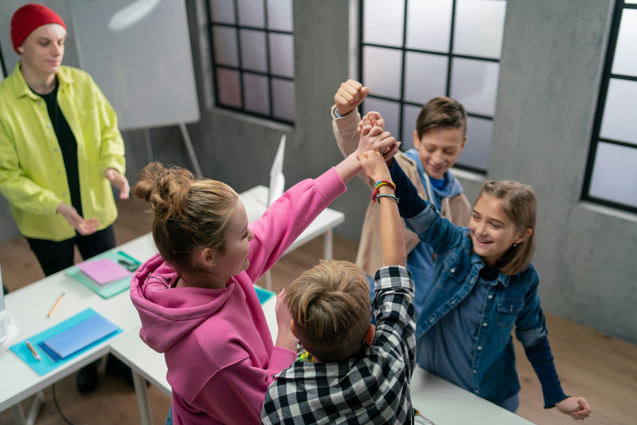 Pupils joining hands in a team high five while their teacher watches