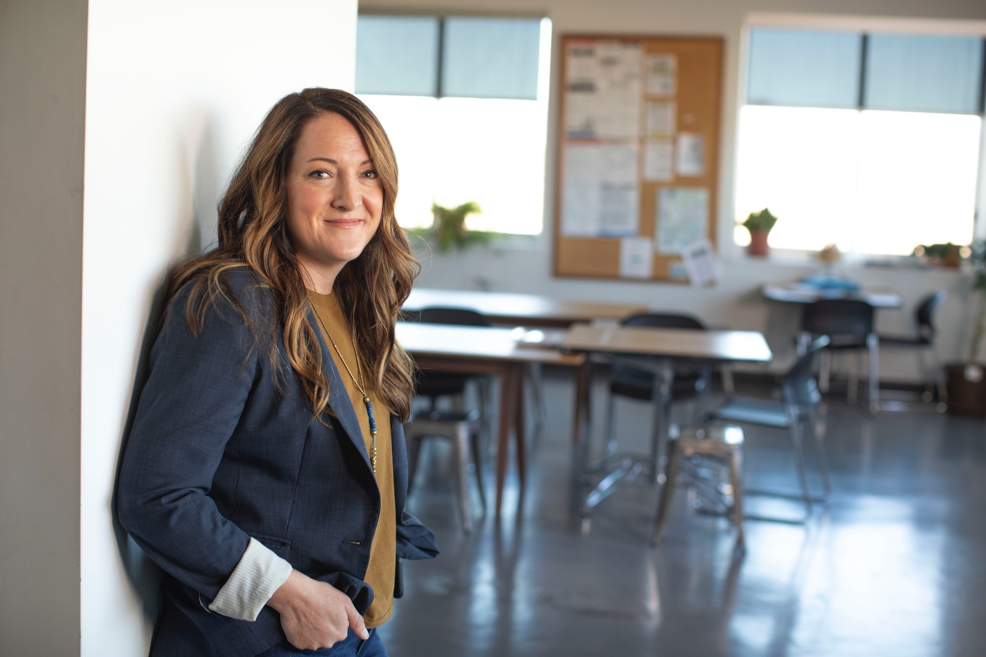Smiling teacher leaning against a wall in an empty classroom