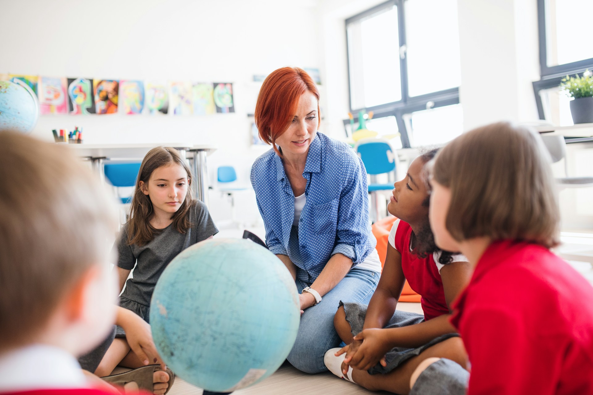 Teacher sitting on the floor with young pupils around a large globe