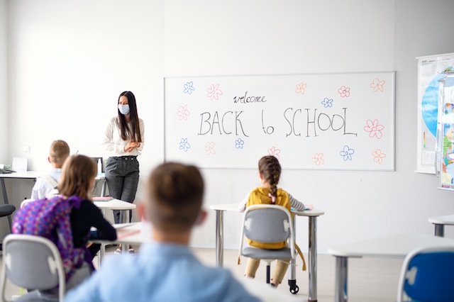 Teacher in a face mask with pupils in a classroom and a Back to school whiteboard